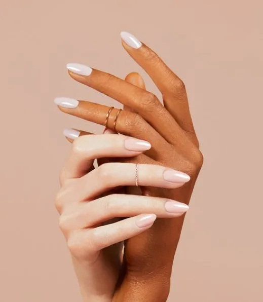 Milky-white almond nails with thin gold rings, clean studio portrait on a warm nude backdrop