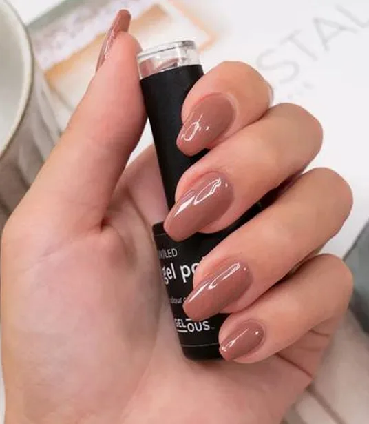Hand with glossy mauve-nude nails holding a gel polish product bottle on warm backdrop