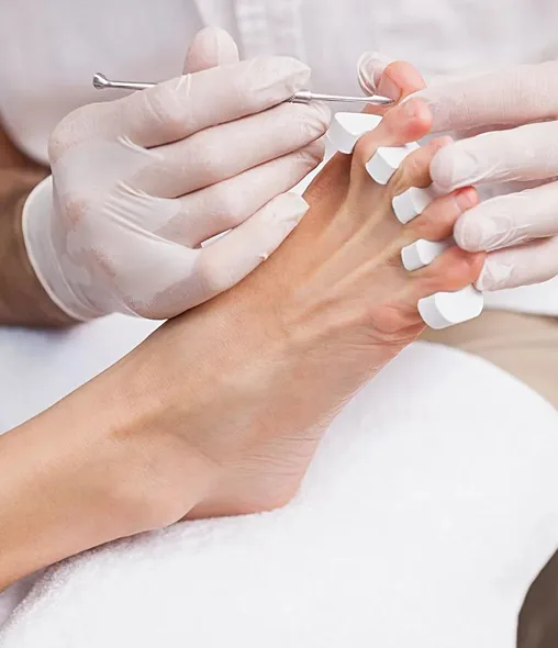 Gloved technician performing a pedicure, toe separators, foot resting on a white towel